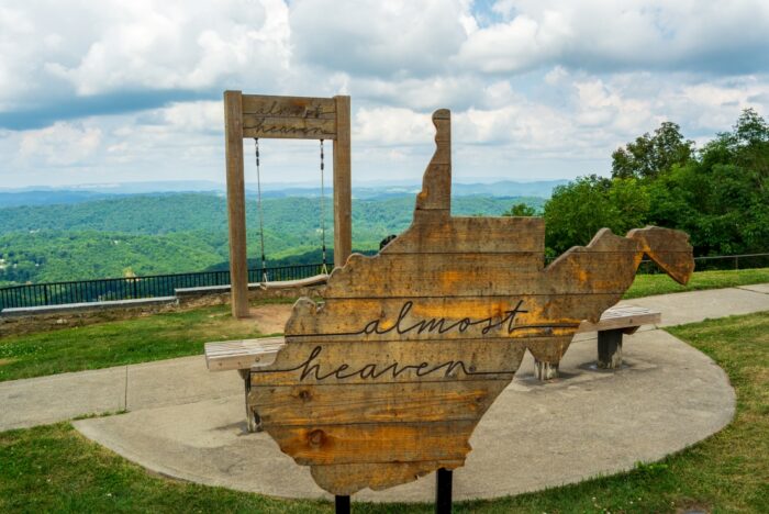 Almost Heaven sign in the shape of West Virginia with a swing at a scenic overlook