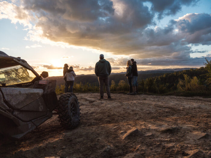 Two couples and a man standing at an overlook watching a sunset with an ATV in the foreground 