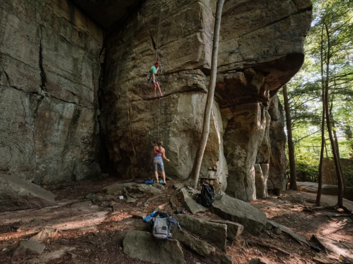  A man climbing a sandstone cliff while a woman watches from below