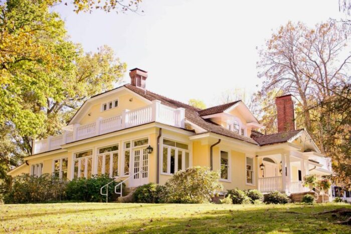 Outdoor photo of The Gaines Estate. Yellow home and green trees surrounding. 