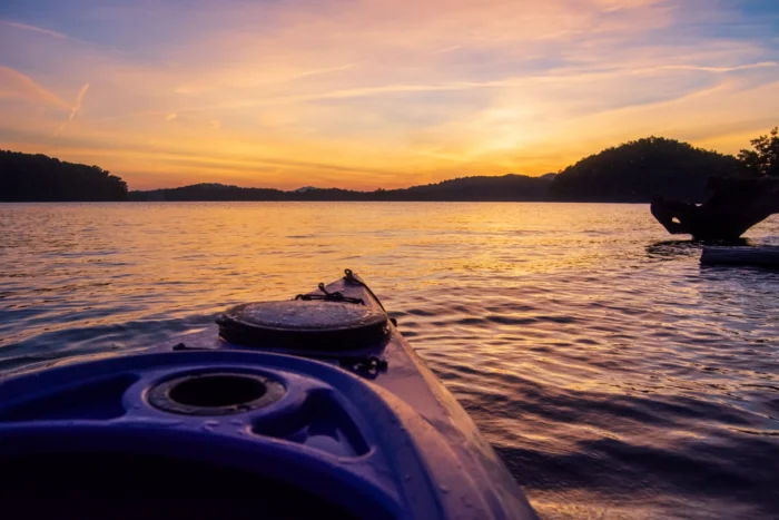 the front of a kayak floating in a lake during a colorful sunset