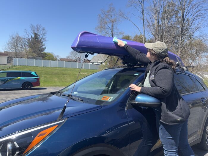 A woman wiping and cleaning her kayak atop of her car