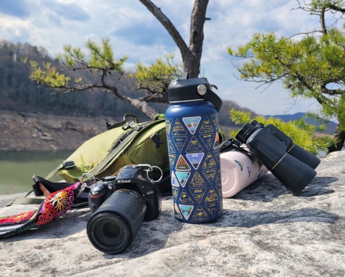 reusable water bottles, camera, binoculars, daypack resting on a rock